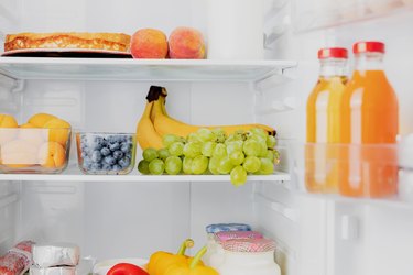 Open fridge or refrigerator door filled with fresh fruits, vegetables, juice