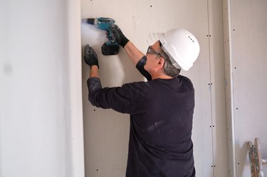 Construction worker assembling plasterboards with screwdriver while working on a construction site.