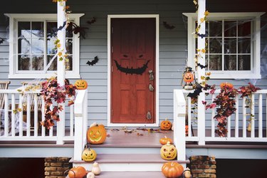 Halloween pumpkins and decorations outside a house with a scary face on the door