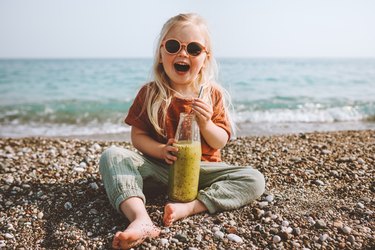 Child drinking smoothie on beach healthy lifestyle summer vacations child with reusable glass bottle vegan organic beverage picnic outdoor kid laughing happy emotions