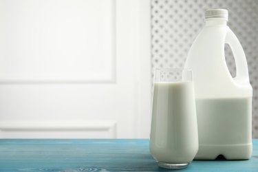 Gallon bottle and glass of milk on blue wooden table. Space for text