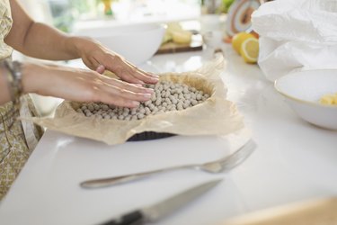 Woman blind baking pie crust with pie weights at kitchen counter