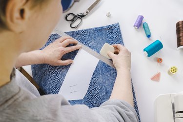 Seamstress marks a piece of clothing on a fabric with a chalk according to a paper pattern