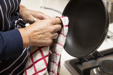 Mature female hand wiping  a frying pan with a tea towel in a domestic kitchen