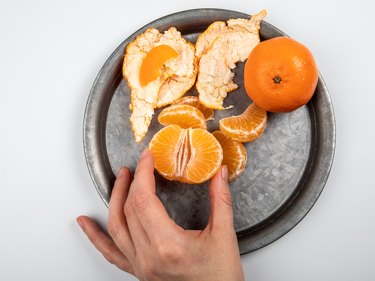 Woman peeling tangerines on a metal plate