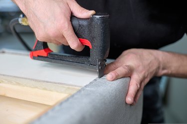 Worker fixes the fabric with a pneumatic stapler in the factory shop.