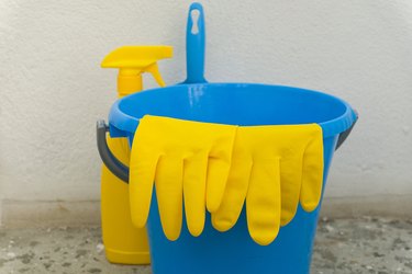 Bottles of detergents, a brush and a dustpan, protective rubber gloves and sponges in a plastic bucket, bright color. Call a cleaning company at home. Professional cleaning after repair or construction.