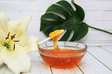 Sugar paste for hair removal in a bowl with lily flower and dracaena leaf in glass vase on white background,  body care