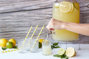 Hand serving fresh lemonade with lemons and lime in the beverage dispenser