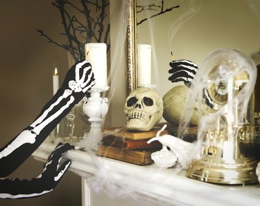 Person dressed in a skeleton costume lights a candles. Halloween composition on fireplace