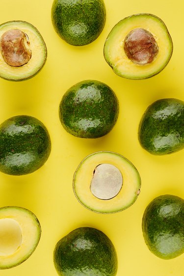 Ripe avocados, some whole and some cut, on yellow background