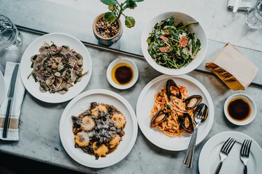 Flat lay of meal for two people with fresh green salad, appetizer, seafood linguine and beef ravioli freshly served on dining table in a restaurant