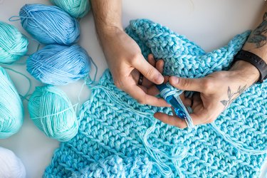 Male hands crochet handmade artwork use wool yarn and hook over table with coffee top view