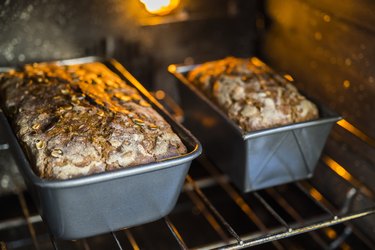 Large and small pans of rye bread with pumpkin and sunflower seeds, shown in the oven and illuminated by the oven light