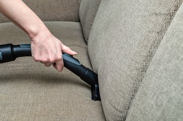 woman vacuums the gray sofa with a washing vacuum cleaner. Cleaning and cleanliness concept