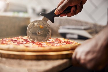 Young man cutting pepperoni pizza on wooden board