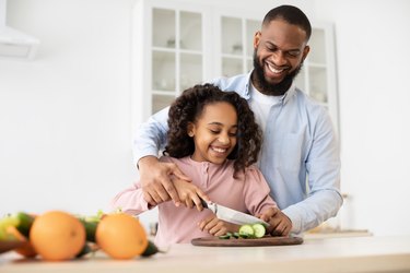 Cheerful african father teaching daughter how to prepare salad