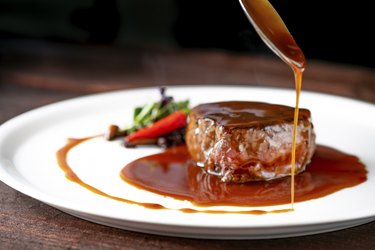 Grilled beef tenderloin steak on a white platter is served with demiglas sauce