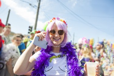 Costumed 20 something girl saying hello and holding phone surrounded by party goers