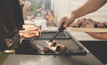 Close up of man grilling food on barbecue grill cooking meat to eat leisure activity