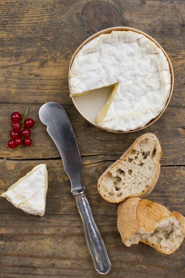 Camembert cheese with red currants and baguette slices on wood table