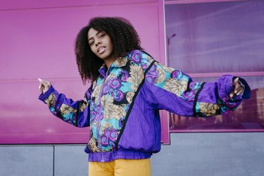 Young woman with urban look dancing in front of pink glass wall