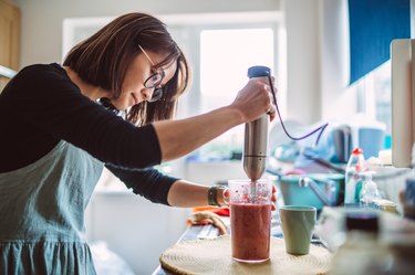 Young pretty woman making fruit smoothie at home