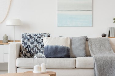 Abstract paste blue and white painting on empty white wall behind beige couch with pillows