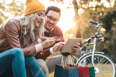 Young couple shopping online with credit card on tablet in public park