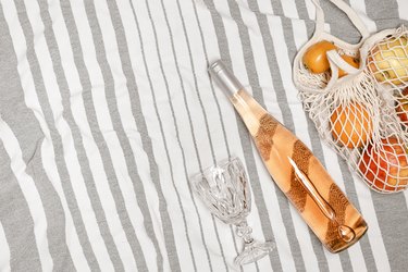 Summer flat lay with bottle rose wine, wine glass, assorted fruits in bag on beach towel as background. Summer beach party, picnic and rest concept. Relaxation at summertime. Top view