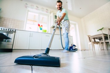 Happy handsome young beard man is cleaning the floor in the domestic kitchen and have fun.