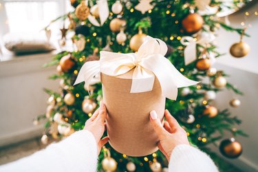 Woman is holding a present against the Christmas tree, close-up first person view