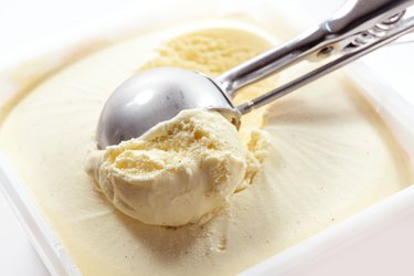 Metal scoop scrapes vanilla ice cream from the box, copy space