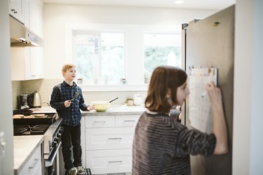 Brother and sister cooking and writing on calendar in kitchen