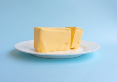 Block of butter on white plate against blue background
