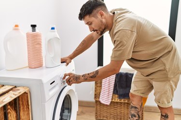 Young hispanic man smilig confident using washing machine at laundry room