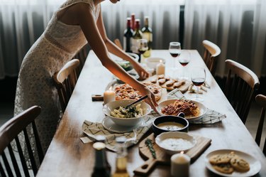 Young Asian woman setting the table and serving food and wine ready for party with friends at home