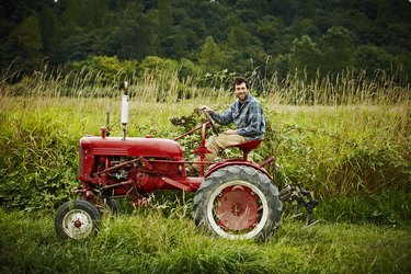 Male farmer driving tractor in field smiling
