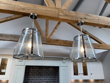 Two glass and chrome pendant lampshades hanging by chains from wooden ceiling beams