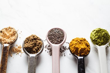 Superfood powders in spoons against white marble background