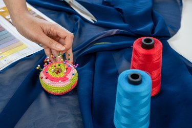 Woman taking pin from pincushion and thread sewing .