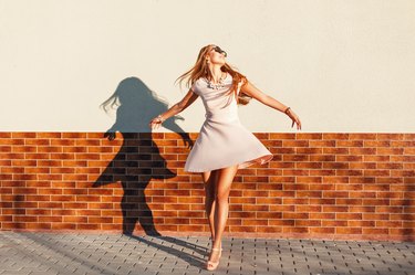 Beautiful young cheerful woman with a smile in a pink dress is spinning around itself near the wall. Happy girl having fun
