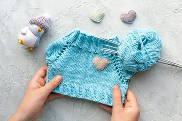 Children's hands holding a knitted T-shirt for a toy made of blue cotton yarn.