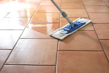 Flat wet-mop made of microfiber wipes the tiled terracotta floor, daily cleaning routine for a hygienic and healthy home, copy space, selected focus