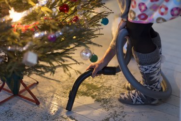 Woman hovering needles under Christmas tree