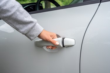 woman's hand opens white car door. partial view of woman opening car door. car unlocks. Business woman opening car door, holding handle. close up