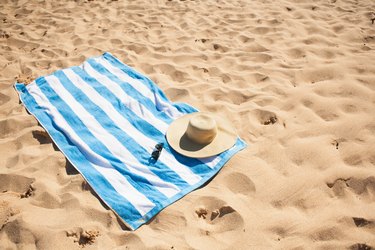 Striped beach towel on sand with hat and glasses