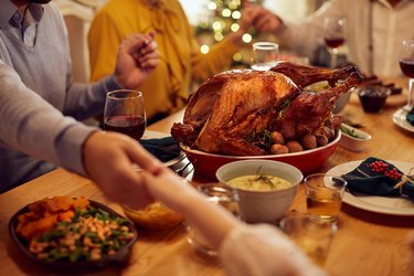 Close-up of family saying grace during Thanksgiving meal at dining table.