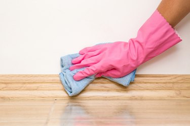Hand in rubber protective glove cleaning baseboard