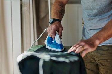 Clothes, iron and hands of man with shirt getting ready in morning for fresh, neat and clean clothing. Housework, laundry and male by ironing board for cleaning, hygiene and domestic lifestyle